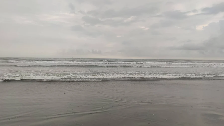 從沙灘遠望海面,海平線附近可見小小的漁船船影