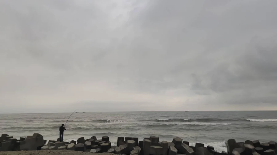 陰天的海邊,有人站在消波塊上釣魚
