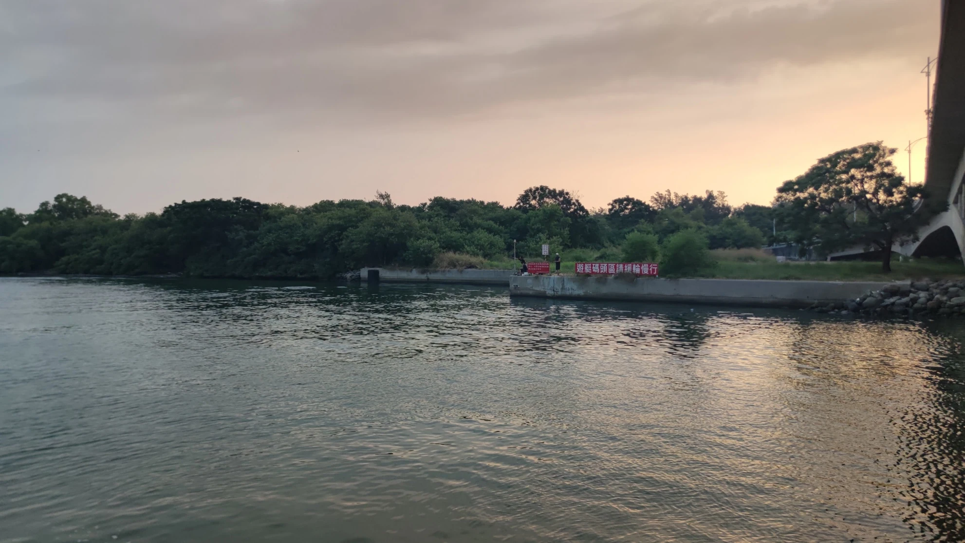 從船上看橋旁岸邊，遠處有人在水邊釣魚