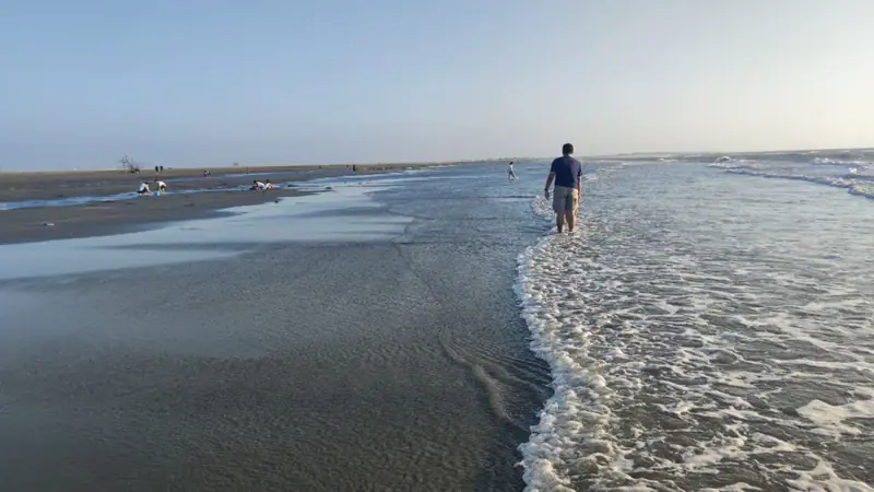 10月10日海灘上有人踏浪，遠方有遊客蹲在濕沙邊