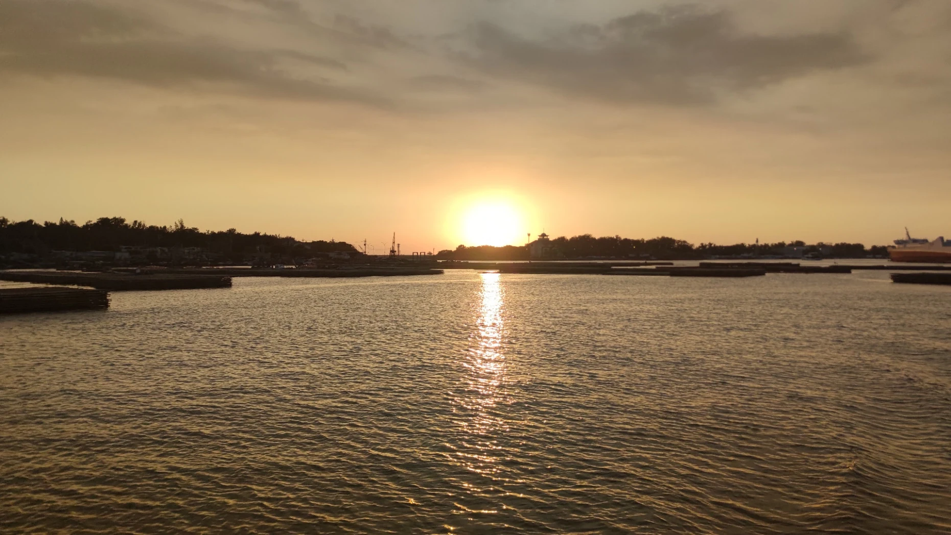 夕陽接近岸線，金色餘暉映照安平港水面