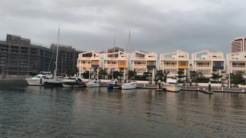 從水面近看岸邊白色房屋，屋前碼頭停著帆船與遊艇