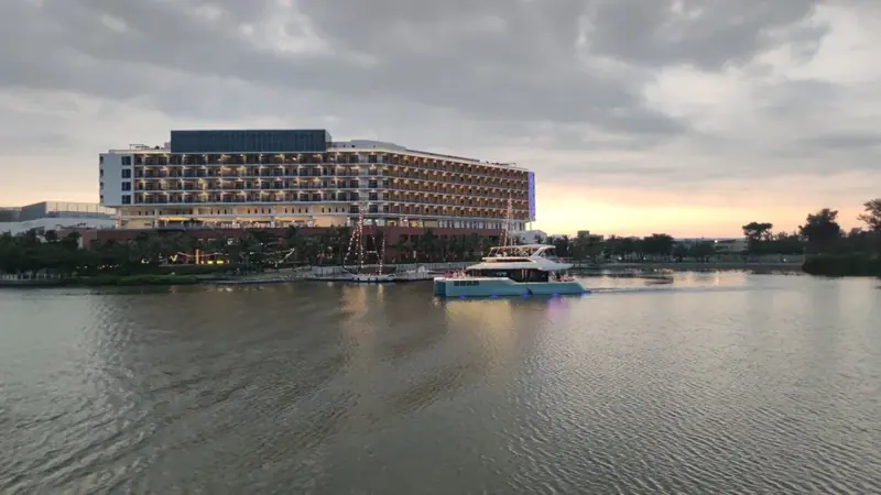 飯店前方有亮起燈光的遊艇，船上可見遊客，水面映出船燈